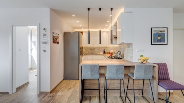 A modern kitchen with a central island, bar stools, pendant lighting, and a view into the adjacent dining area. - Bells & Whistles, Comfortable Condo (Split)