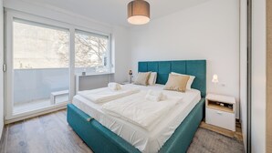 A modern bedroom with a large bed, a teal headboard, and a bedside table with a lamp. - Bells & Whistles, Comfortable Condo (Split)