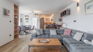 A modern living room with a grey sectional sofa, a wooden coffee table, and a dining area with a purple chair and a wooden bookshelf. - Bells & Whistles, Comfortable Condo (Split)