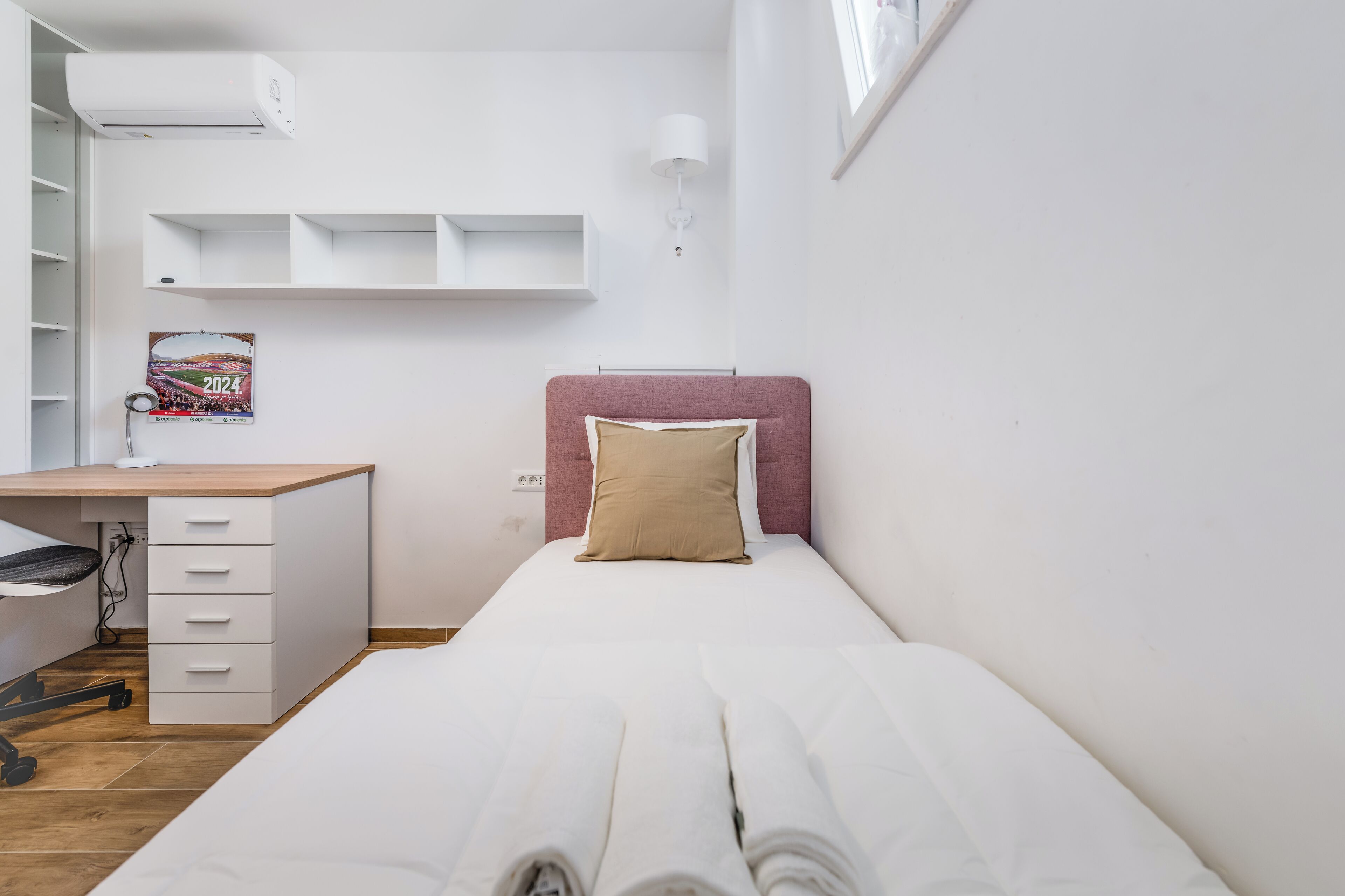 Um quarto pequeno e bem organizado, com uma cama, uma escrivaninha e uma cadeira.