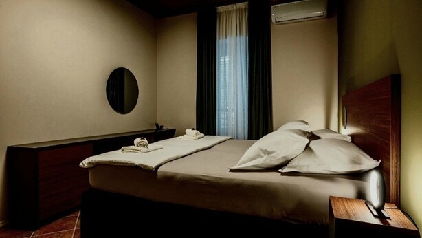 A hotel room with a bed, bedside table, and a mirror on the wall.