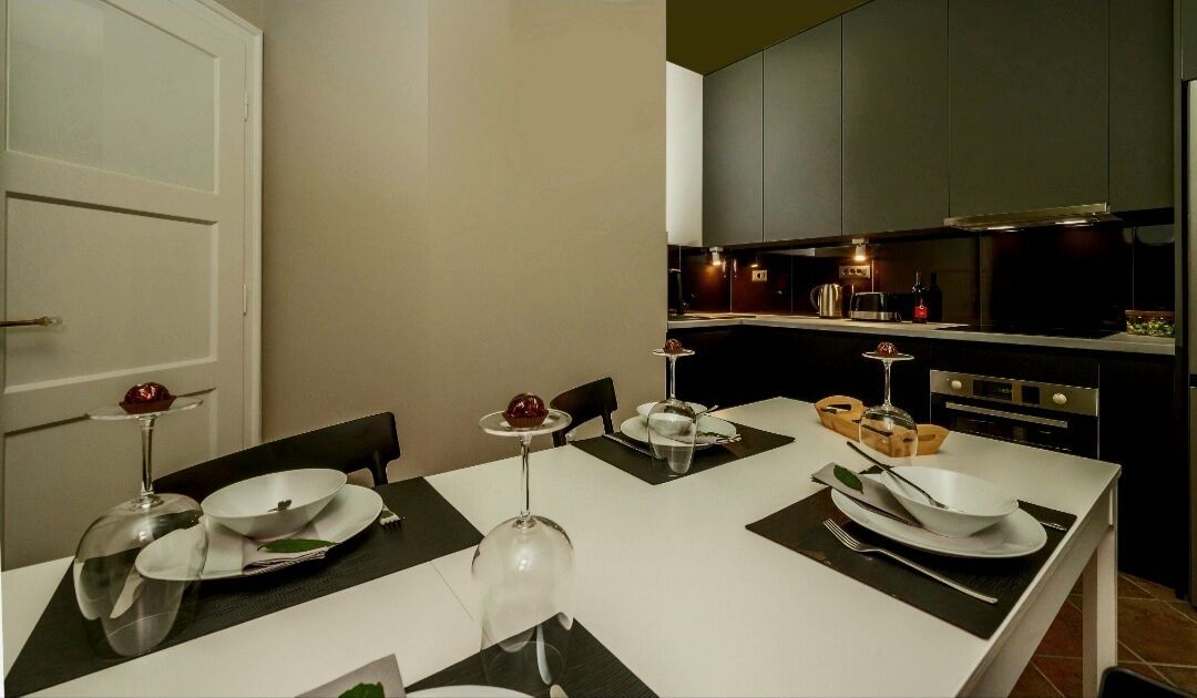 Una cocina moderna con armarios oscuros, una encimera blanca y una zona de comedor con una mesa dispuesta para cuatro.