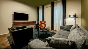 A modern living room with a grey sofa, a black armchair, a small round table, and a flat-screen TV mounted on the wall.