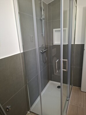 A glass-enclosed shower stall with a chrome showerhead and handle, tiled walls, and a white door. - Hill Pool House, Kaštel Kambelovac Retreat (Kaštel Kambelovac)