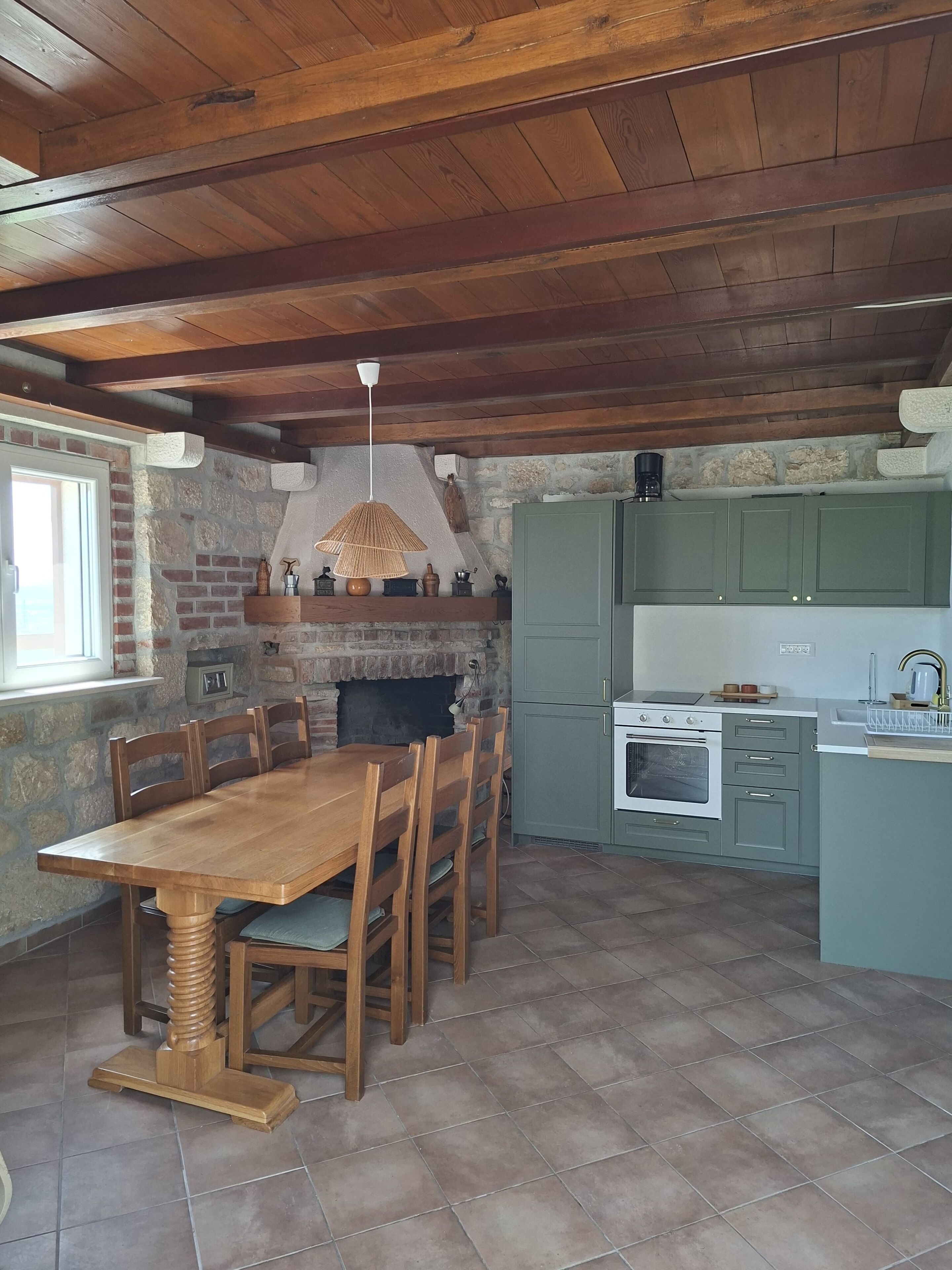 A rustic kitchen with a stone wall, wooden ceiling, and a dining table with chairs.