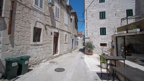 A narrow street with stone buildings, a small outdoor seating area, and a trash bin. - Kira, One Bedroom Apartment In Old Town (Split)