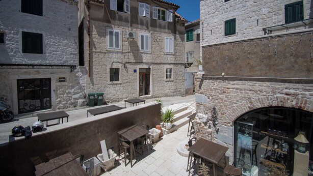 A courtyard with outdoor seating, stone buildings, and a shop with glass display. - Kira, One Bedroom Apartment In Old Town (Split)