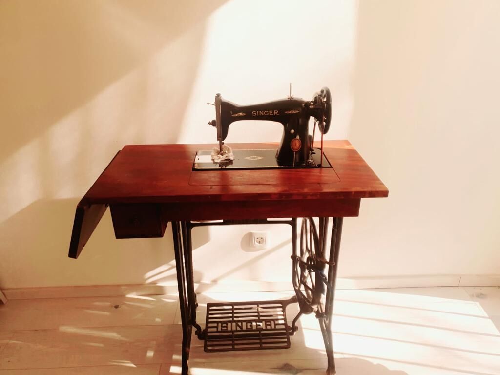 Een Singer naaimachine op een houten tafel met een metalen voetsteun.