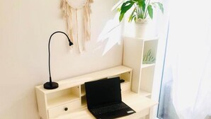 A minimalist workspace with a wooden desk, a laptop, a dreamcatcher, a potted plant, and a round ottoman. - Koko&Friends, Charming Place In Quite Neighborhood (Split)