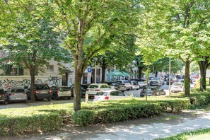 A street lined with parked cars and trees, with buildings in the background.