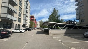 Een parkeerplaats met auto's, een overdekt gedeelte en meerhoogbouw op de achtergrond.