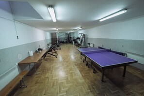 A gym with exercise equipment, a ping pong table, and benches.