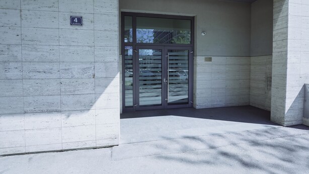 Een gebouwentree met een glazen deur, een bord met het cijfer '4' en een betonnen muur.