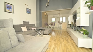 Un salon moderne avec un canapé gris, une table basse et, au fond, un coin repas.