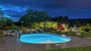 Une piscine avec des chaises longues et un kiosque dans un jardin.