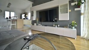 Un salon moderne avec une table basse en verre, un canapé gris et un meuble de télévision blanc doté d’un écran plat.