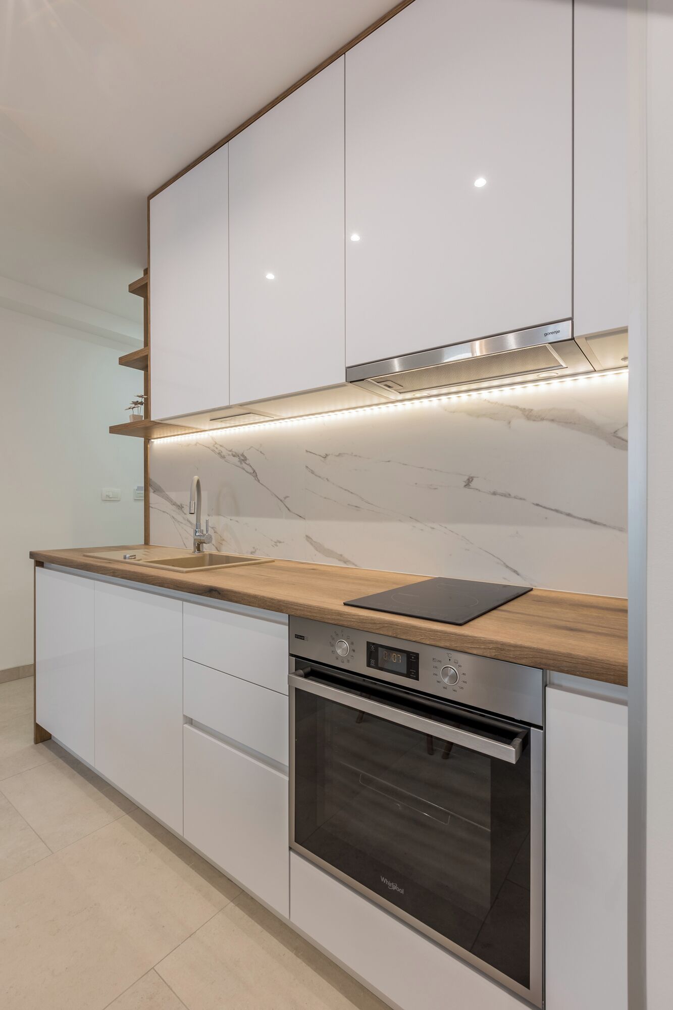 A modern kitchen with white cabinets, a wooden countertop, a built-in oven, and a stainless steel range hood.