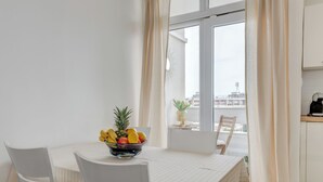 A dining area with a white table and chairs, a bowl of fruit, and a view of the city through large windows. - Vuvuzela Bay, Three-Bedroom Apartment (Split)