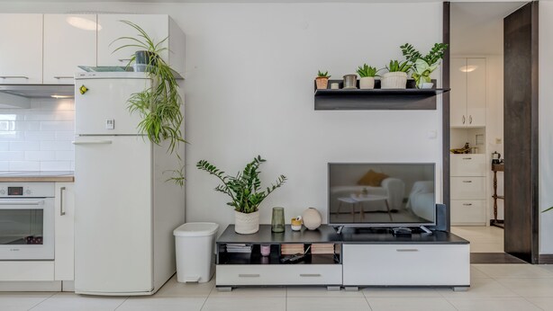 A modern kitchen with white cabinetry, a built-in oven, a refrigerator, and a dining area with a white chair and table. - Vuvuzela Bay, Three-Bedroom Apartment (Split)