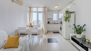 A modern kitchen with white cabinets, a dining area with a table and chairs, and a living area with a sofa and a plant. - Vuvuzela Bay, Three-Bedroom Apartment (Split)