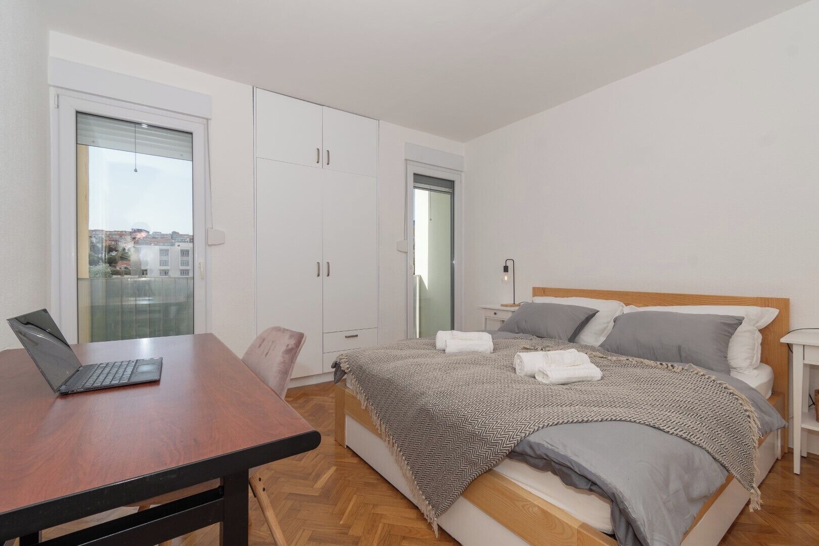 A bedroom with a bed, a desk with a laptop, a wardrobe, and a nightstand.