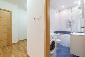 A bathroom with a washing machine, toilet, and a glass shower enclosure. - Zozo, Modern Two-Bedroom Suite (Split)