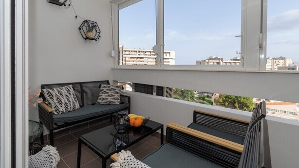 A balcony with a black sofa, a glass coffee table, and a small fruit bowl. There are two hexagonal wall decorations with plants. - Zozo, Modern Two-Bedroom Suite (Split)