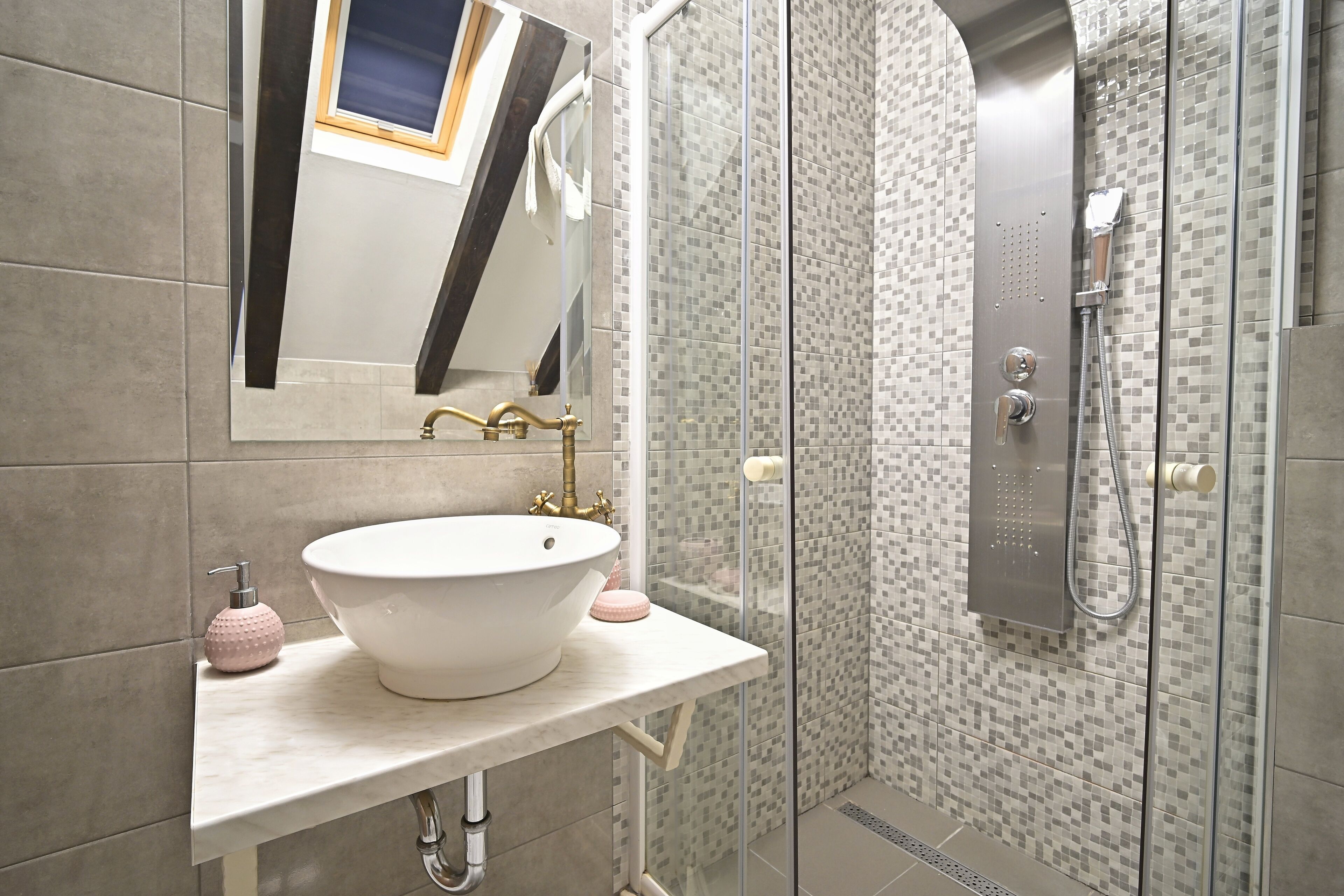 Un bany amb un lavabo blanc, un mirall, una dutxa amb porta de vidre i parets revestides de rajoles.
