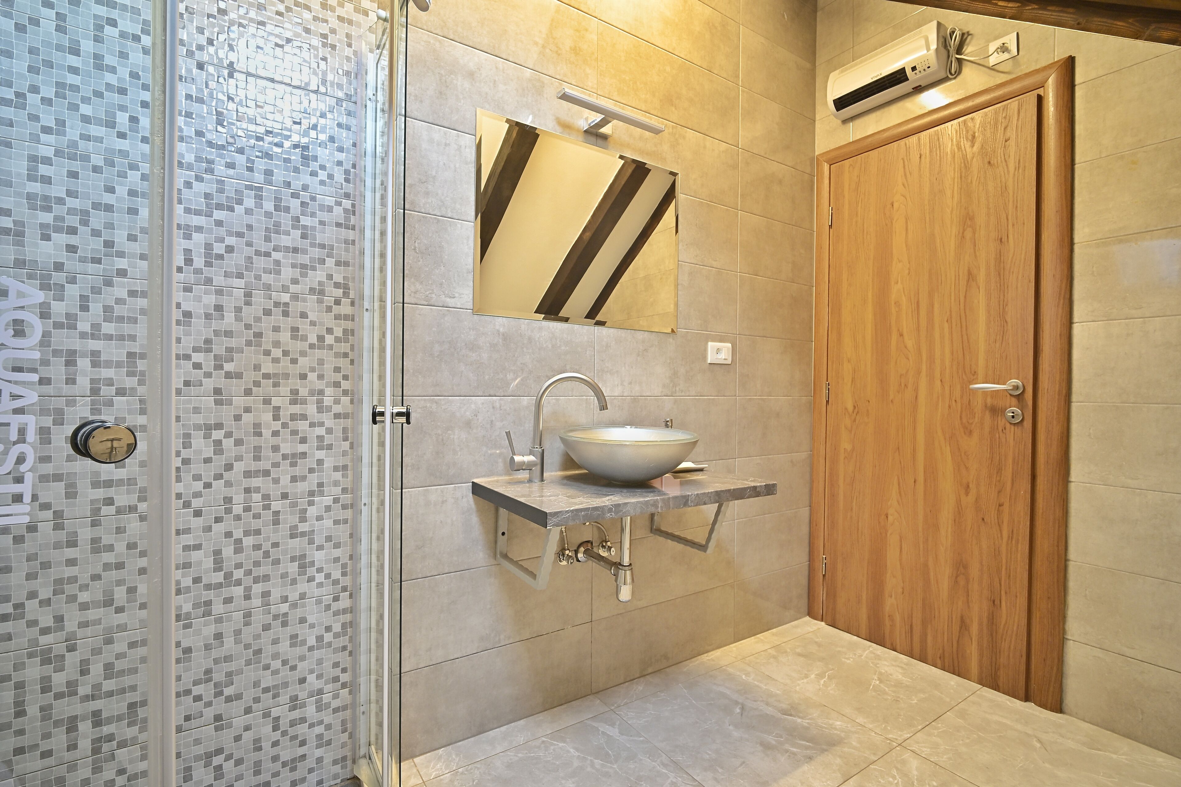 Un baño con cabina de ducha de vidrio, un lavabo con lavataza, una puerta de madera y un salpicadero de azulejos.