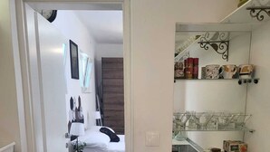 Een kleine keuken met een fornuis, een eethoek met een tafel en stoelen, en een slaapkamer met een bed en nachtkastje.