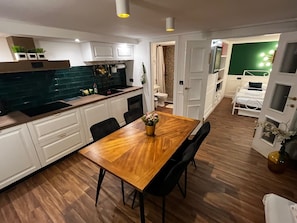 A modern kitchen with white cabinets, a wooden dining table, and black chairs. There is a small plant on the table.