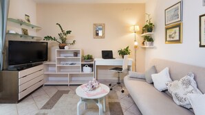 A modern living room with a flat-screen TV, a desk with a laptop, a white sofa, and decorative plants. - Arca, Apartment With Sea View And Free Parking (Podstrana)
