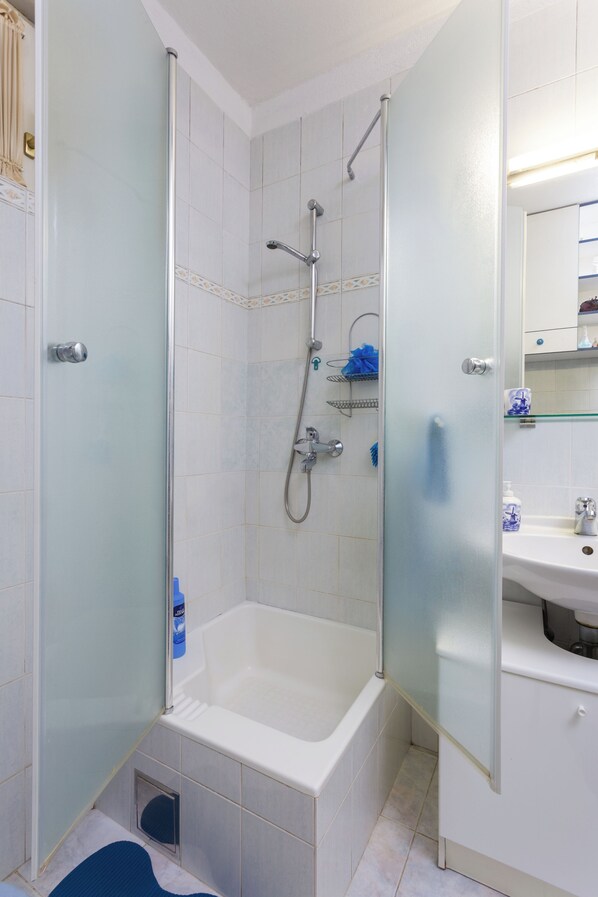Une salle de bain moderne avec une douche à parois de verre, une baignoire blanche et un lavabo surmonté d’un miroir.