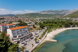 Une ville côtière avec une plage, une rue bordée de voitures garées et un immeuble à plusieurs étages.