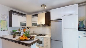 A modern kitchen with white cabinets, a stainless steel refrigerator, a gas stove, and a microwave. There is a fruit bowl on the counter and a clock on the wall. - Arca, Apartment With Sea View And Free Parking (Podstrana)