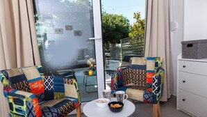 Una habitación con dos sillones coloridos, una mesita blanca con un cuenco y una taza, y un armario blanco.