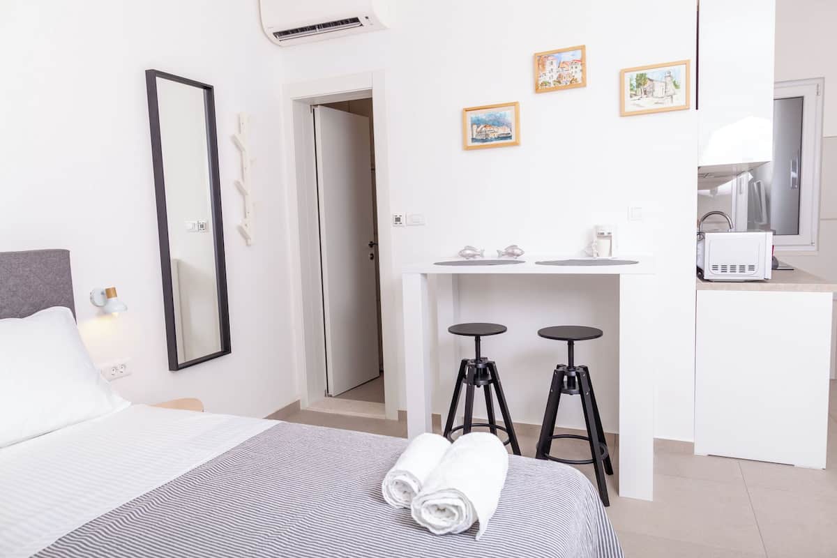 Une chambre d’hôtel comprenant un lit, un bureau, deux tabourets, un miroir et une kitchenette.