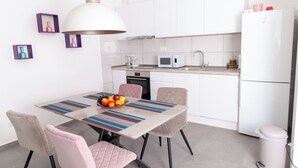 Cocina moderna con armarios blancos, microondas y pileta. Hay una mesa de comedor con sillas y un frutero encima.