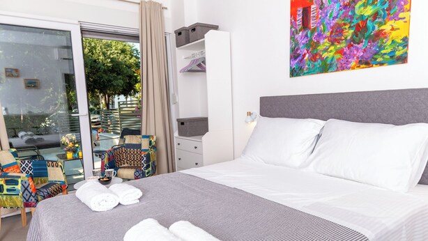 Habitación de hotel con cama, ventana con cortinas, un cuadro abstracto colorido y un armario con estantes.