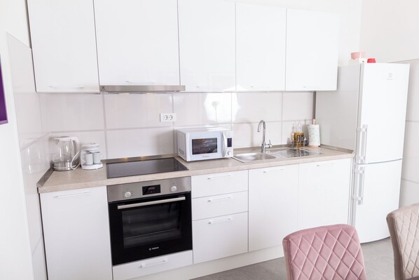 A modern kitchen with white cabinets, a microwave, a stove, and a refrigerator. - Apartments Bilić (Split)