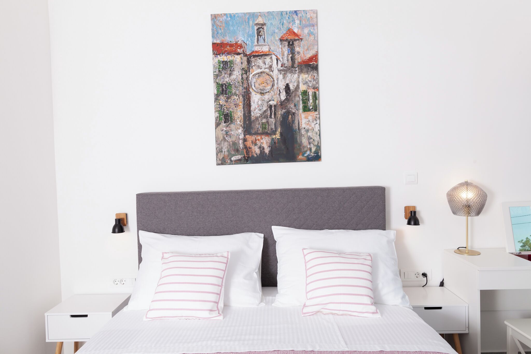 A bedroom with a bed, white nightstands, a desk, and a wall-mounted lamp.
