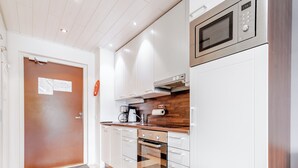 A modern kitchen with white cabinets, a stainless steel microwave, a built-in oven, and a wooden backsplash. - Modern 1BR Apartment next to Ski Slopes (Sirkka)