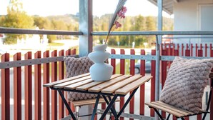 A wooden table with a white vase and pink flowers, two cushioned chairs, and a red and white fence in the background. - Modern 1BR Apartment next to Ski Slopes (Sirkka)