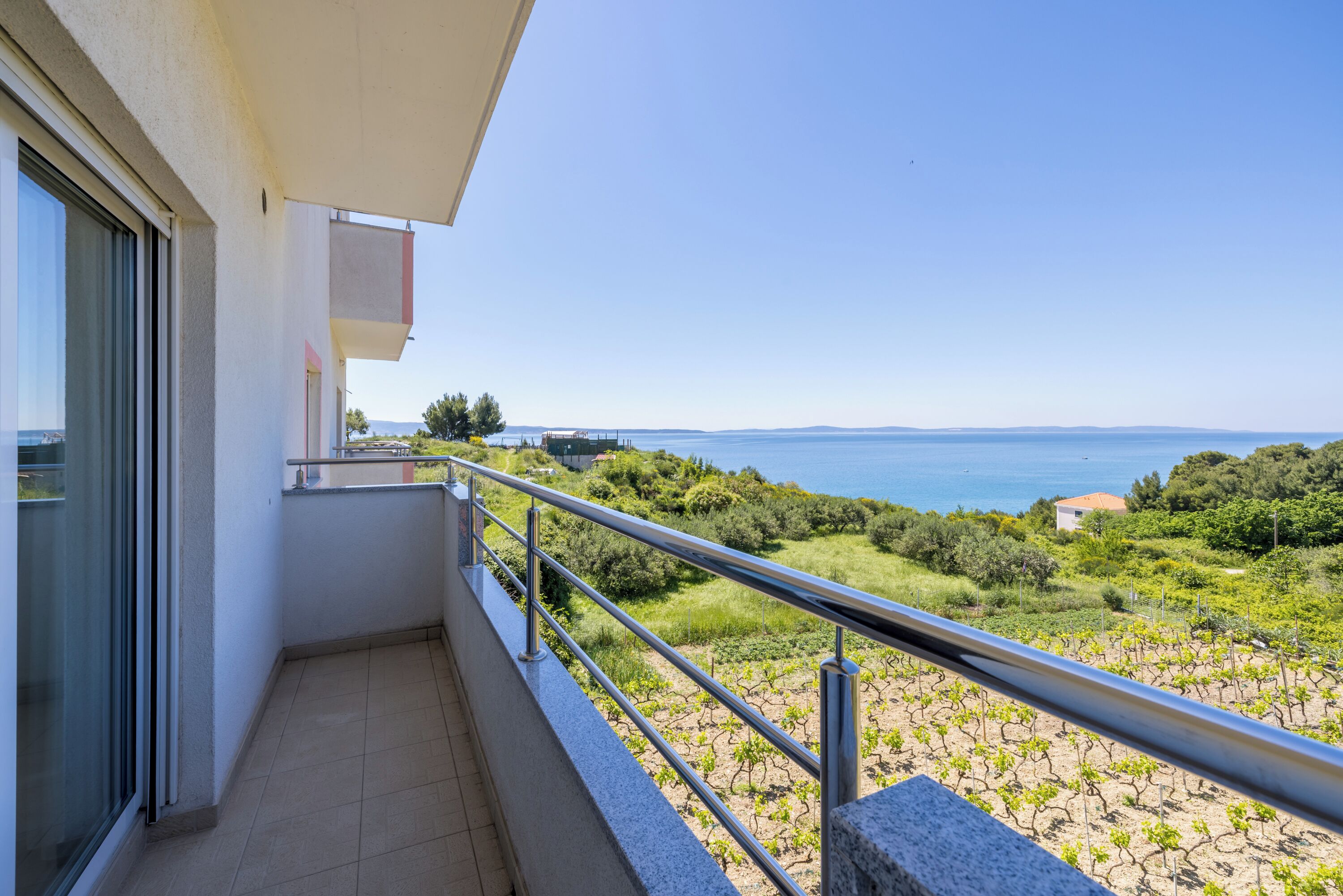 A balcony with a metal railing overlooking a vineyard and a body of water.
