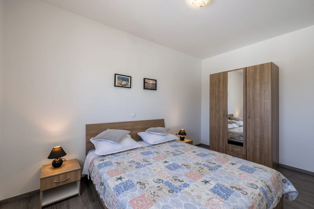 Ein Schlafzimmer mit einem Bett, zwei Nachttischen mit Lampen, einem Kleiderschrank und zwei gerahmten Bildern an der Wand.