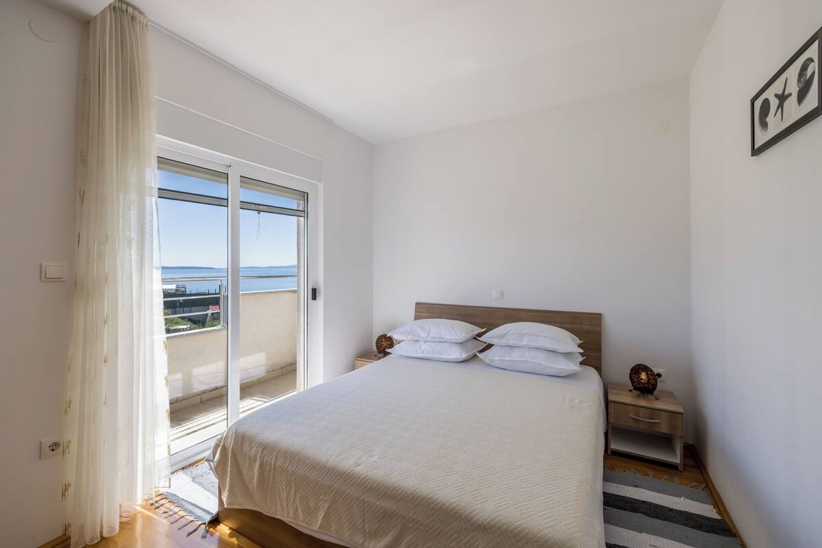 Ein Schlafzimmer mit Bett, Nachttisch, Fenster mit Vorhängen und Blick ins Freie.