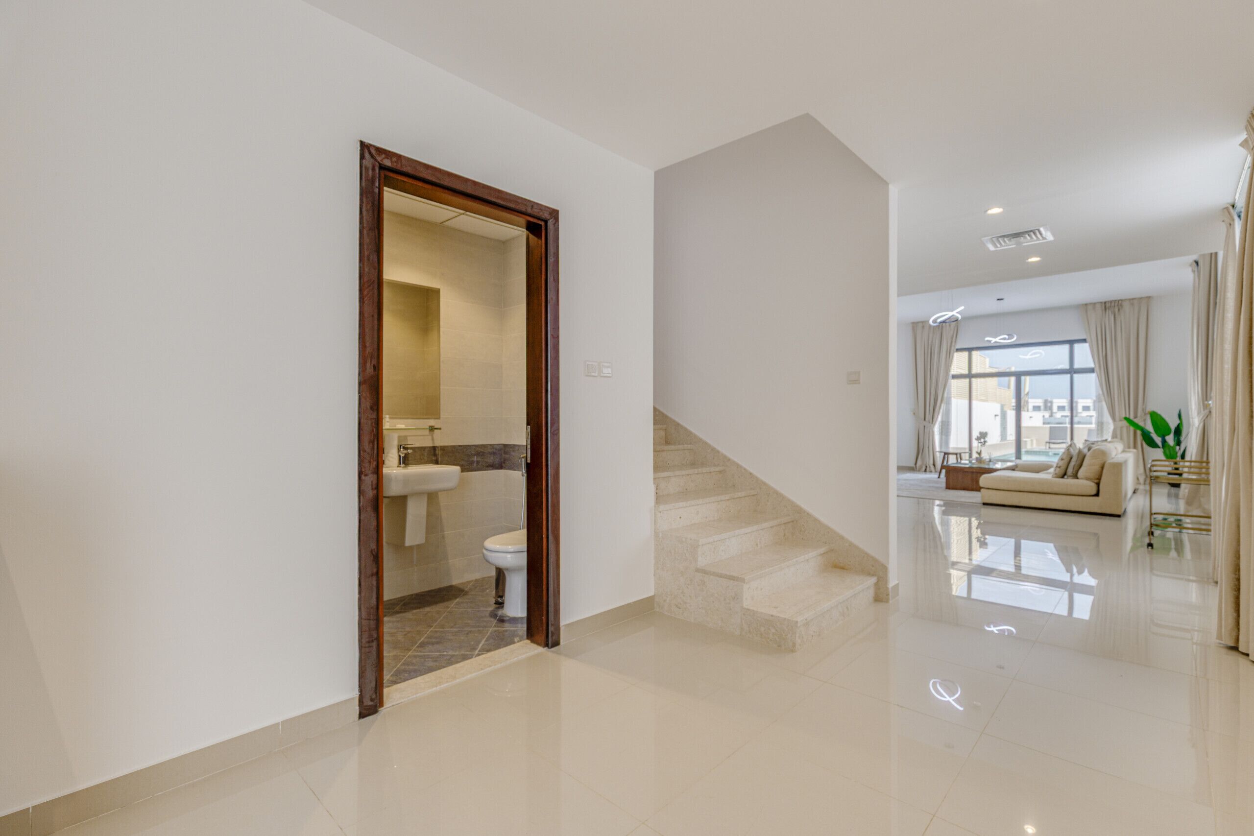 A spacious living area with a staircase leading to a balcony, a modern bathroom with a toilet and sink, and a large window with curtains.