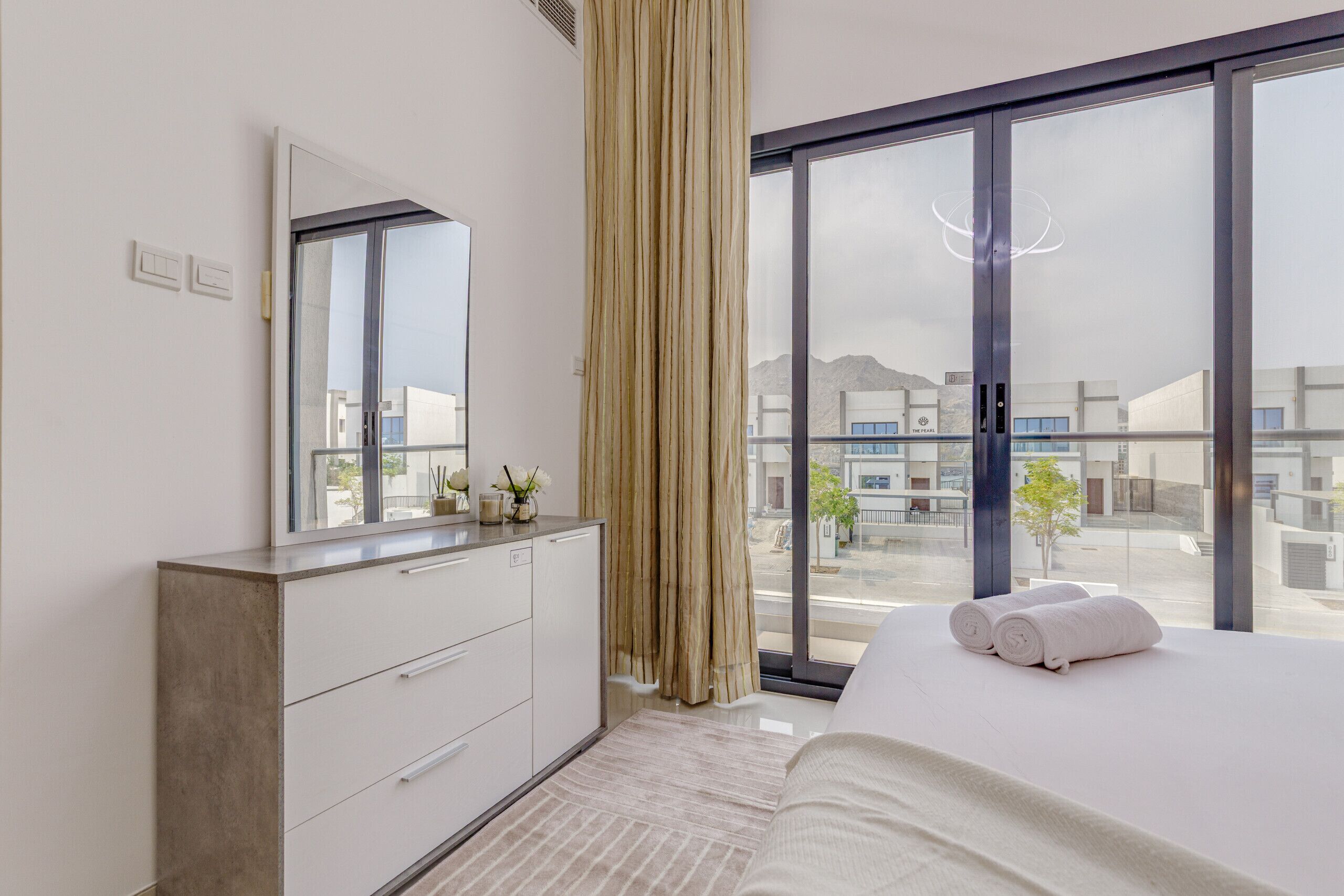 Une chambre d’hôtel moderne, dotée d’un grand lit, d’une commode, d’un miroir et offrant une vue sur la ville grâce à de grandes fenêtres.