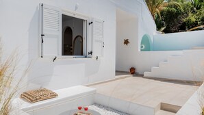A modern outdoor seating area with a white wall, a small table with drinks, and a decorative bowl.