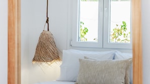 A bedroom with a bed, a hanging light fixture, and a window with a view of greenery.